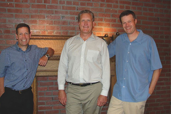 Three smiling men in button up shirts.