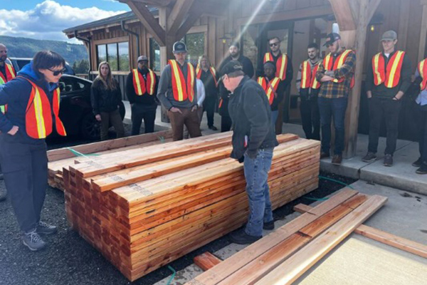 People in safety vests work with large shipment of lumber