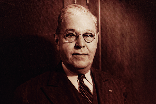 Joe Erceg historical photo with his glasses on in a suit