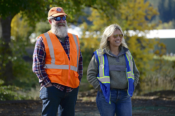 Two people in safety vests outside, watching work.